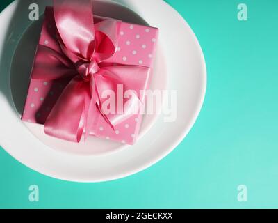 A gift box with a pink ribbon lies on the plates saucers on a mint-colored background Stock Photo