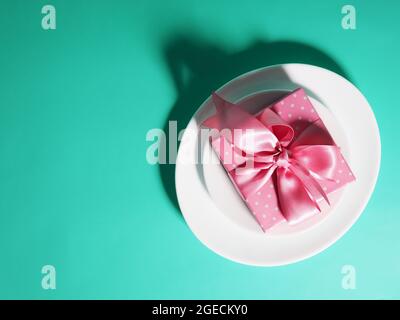 A gift box with a pink ribbon lies on the plates saucers on a mint-colored background Stock Photo