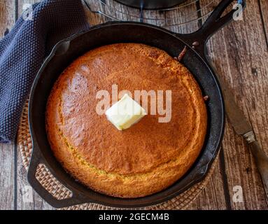 Fresh baked homemade cornbread in a rustic cast iron pan on wooden table background. Closeup and isolated view Stock Photo
