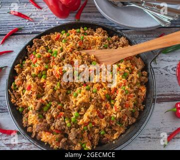 Pan dish with Serbian djuvec rice with minced meat served isolated  in rustic cast iron pan with spatula on light wooden background. Table top view Stock Photo