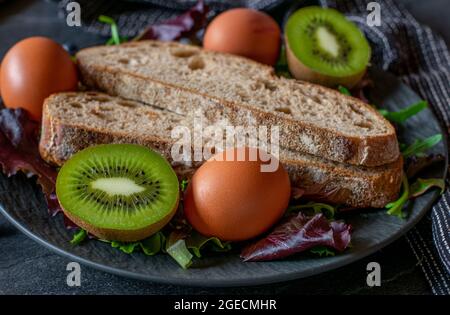 A plate with vegetarian food such as organic boiled eggs, sourdough bread and fresh halved kiwis. Closeup view on dark background Stock Photo