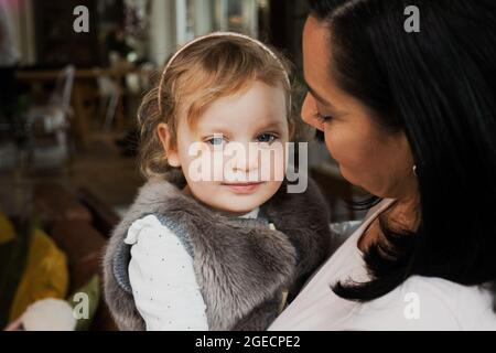 Close up of beautiful daughter being held by mother in modern kitchen. Stock Photo
