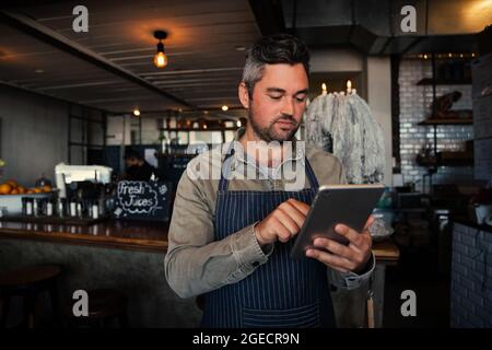 Caucasian waiter scrolling through online menu standing in trendy cafe preparing orders. Stock Photo