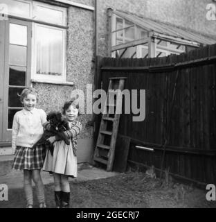 1950s, historical, two excited young girls in a back yard of a terraced house, one holding their puppy, England, UK Stock Photo