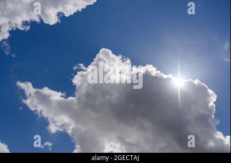 Fluffy white clouds passing in front of the sun in a bright blue sky. Stock Photo