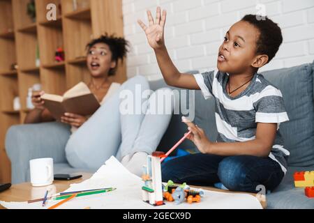 Black joyful woman reading book and having fun with her son at home Stock Photo