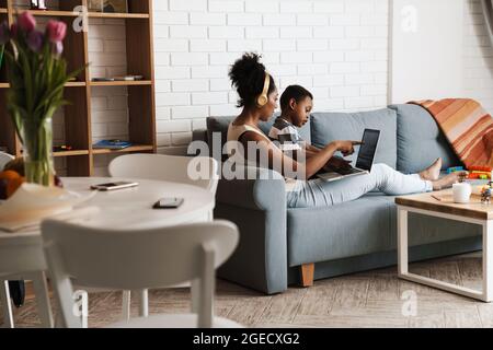 Black mother and son using laptop while sitting on sofa at home Stock Photo