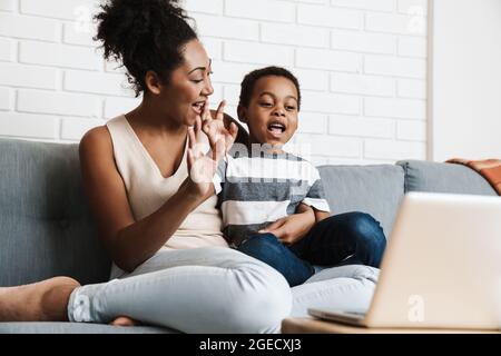 Black happy mother and son gesturing while using laptop at home Stock Photo