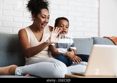 Black happy mother and son gesturing while using laptop at home Stock Photo