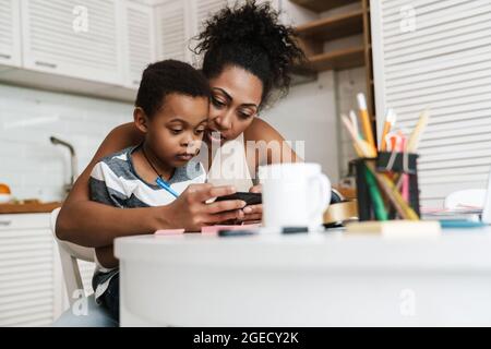 Black mother and son using mobile phone while sitting together at home Stock Photo