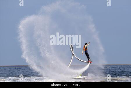 an artist is performing  flying trapeze show on the sea. Stock Photo