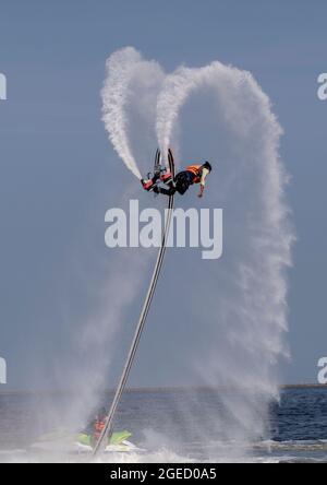 an artist is performing  flying trapeze show on the sea. Stock Photo