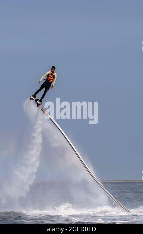 an artist is performing  flying trapeze show on the sea. Stock Photo