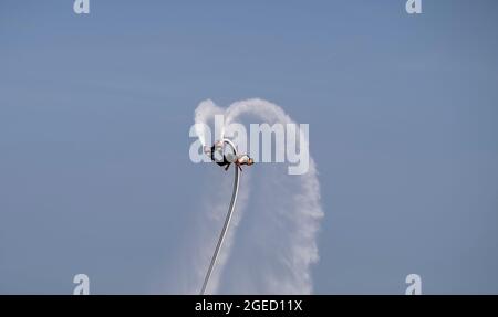 an artist is performing  flying trapeze show on the sea. Stock Photo