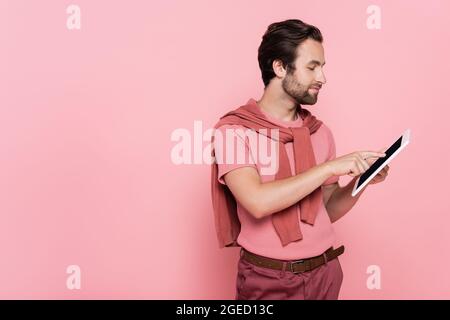 Side view of man with jumper on shoulders using digital tablet isolated on pink Stock Photo