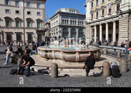 ROME, ITALY - APRIL 10, 2012: People sit by the fountain at Piazza Colonna square in Rome. According to official data Rome was visited by 12.6 million Stock Photo