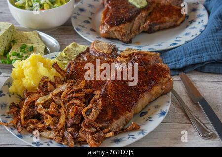 organic and dry aged  irish T-bone or porterhouse steak with deep fried onions, mashed potatoes and salad on a plate Stock Photo
