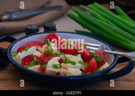 Traditional homemade tomato salad with buffalo mozzarella, olive oil and chives. Served in a bowl with fork on rustic and wooden table Stock Photo