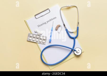 Clipboard with text HEARING PROBLEMS, stethoscope and pills on color background Stock Photo