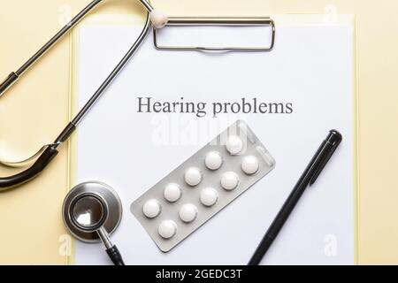 Clipboard with text HEARING PROBLEMS and pills on color background Stock Photo