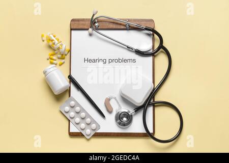 Clipboard with text HEARING PROBLEMS, stethoscope and pills on color background Stock Photo