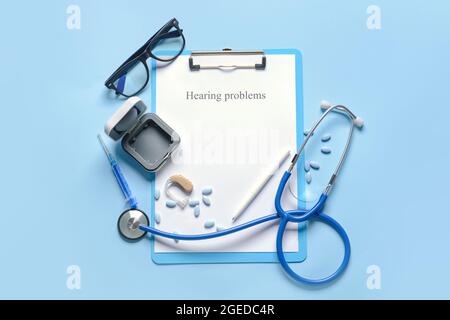 Clipboard with text HEARING PROBLEMS, stethoscope and pills on color background Stock Photo