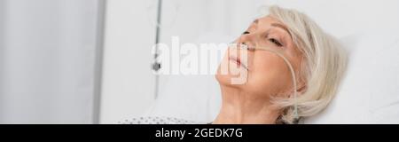 Senior woman with nasal cannula lying on bed in hospital, banner Stock Photo