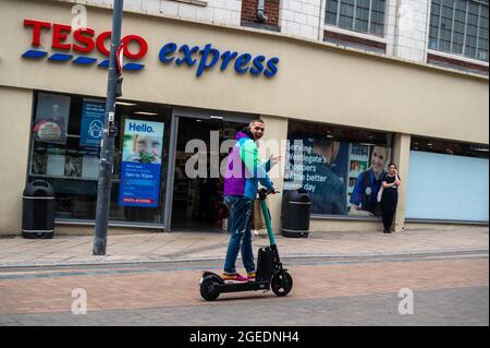 Young man smiling and waving on a Beryl E scooter travelling up Westlegate norwich outside Tesco express Stock Photo