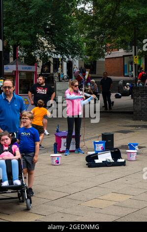 Young Lady playing an electric violin in the middle of Norwich city centre with cancer research Uk buckets for people to put cash into Stock Photo