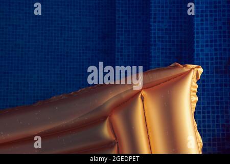 Golden swimming mattress in the pool against blue water on sunset. Vacation and holidays concept photo. Free space. Closeup view from above. Stock Photo