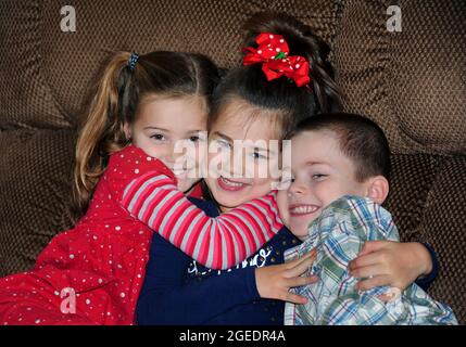 One brother and two sisters group hug on a sofa in their home.  They have huge grins on their face and beam happiness and love. Stock Photo