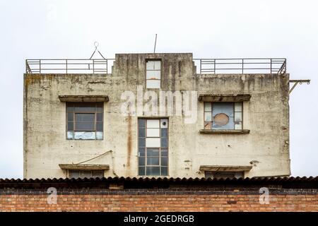 A derelict building with boarded and broken windows stands isolated behind a brick wall. Stock Photo