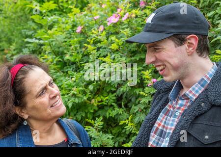 A middle aged woman looks confused as a yoinger man pulls a face and laughs. Stock Photo