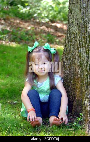 Beautiful little girl wiggles her toes as she enjoys going barefoot on a Tennessee afternoon.  She has pigtails and bright green ribbons. Stock Photo