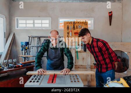 Senior carpenter teaching a younger man how to work Stock Photo