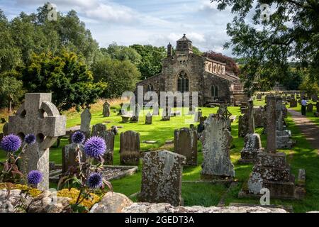 Woman walking through St Michael and All Angels Church grounds with foreground flowers, Linton village, Grassington, Wharfedale, Yorkshire Dales UK Stock Photo