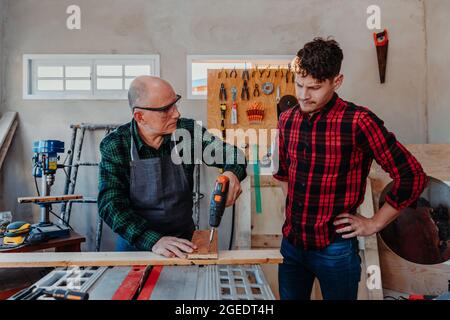 Senior carpenter teaching a younger man how to work Stock Photo