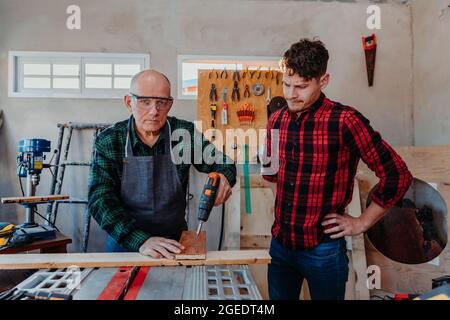 Senior carpenter teaching a younger man how to work Stock Photo