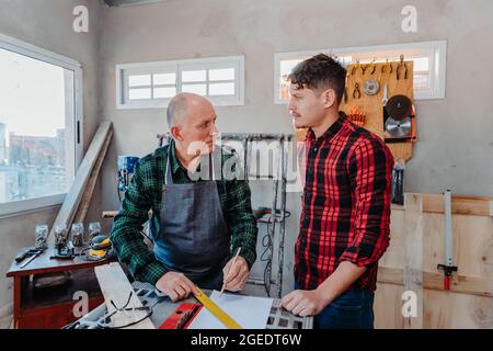 Senior carpenter teaching a younger man how to work Stock Photo