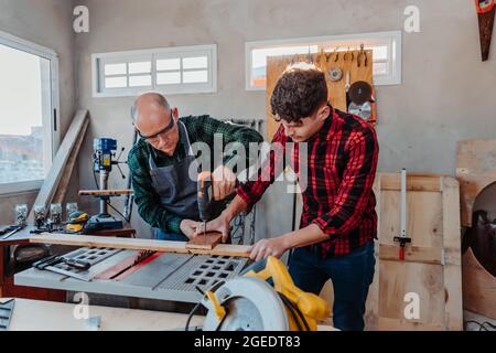 Senior carpenter teaching a younger man how to work Stock Photo