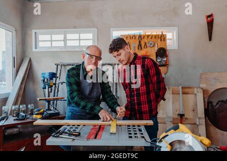 Senior carpenter teaching a younger man how to work Stock Photo
