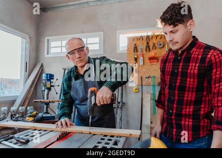 Senior carpenter teaching a younger man how to work Stock Photo