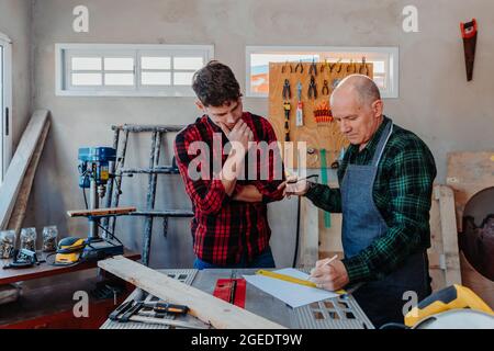 Senior carpenter teaching a younger man how to work Stock Photo
