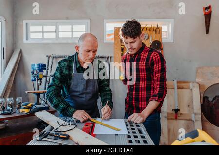 Senior carpenter teaching a younger man how to work Stock Photo