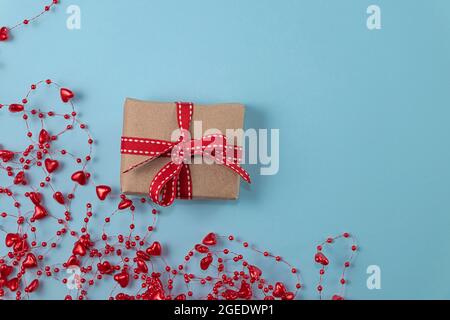 concept of minimalism valentine's day. gift with red ribbon on pastel blue background with red beads with hearts with copy space. Soft focus. flat lay Stock Photo