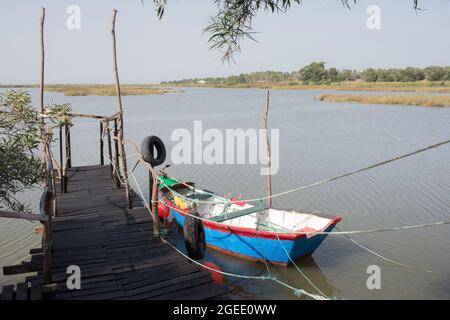 Peaceful landscape with a blue boat next to a wooden pier. Rice fields in the distance. Comporta, Portugal, Europe. Stock Photo