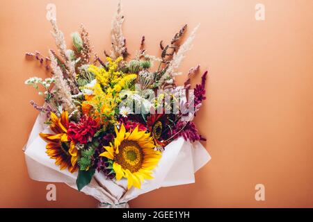 Fall bouquet of yellow red orange flowers wrapped in paper and arranged on brown background. Sunflowers, amaranth, daisies with zinnias and grasses Stock Photo