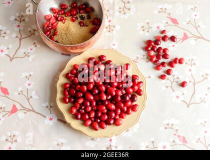 Fresh cranberries in a wooden bowl on a red snowflake Christmas napkin, with loose berries scattered on a floral tablecloth, viewed from above Stock Photo