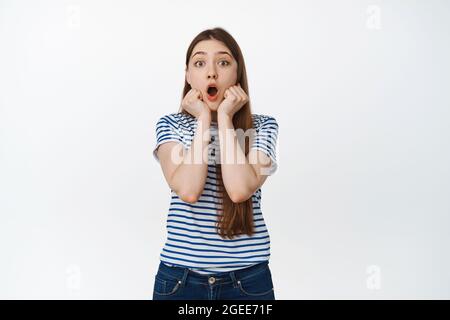 Impressed young woman staring in awe with dropped jaw, watching excited, hold hands near face with surprised emotion, white background Stock Photo