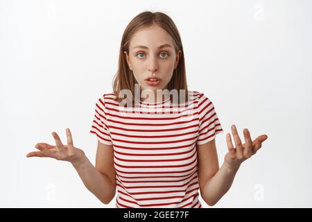 What wrong. Confused blond teen girl shrugging, raising hands and look puzzled, cant understand what happened, asking question, staring clueless at Stock Photo